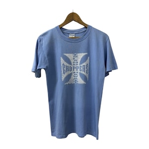 May include: Light blue t-shirt with a white graphic of a Maltese cross and the word "Choppers" in a stylized font. The shirt is hanging on a wooden hanger against a white background. The t-shirt is made of a soft material.
