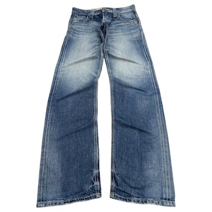 Puede incluir: Vaqueros azules de mezclilla con un lavado descolorido. Los vaqueros tienen un diseño clásico de cinco bolsillos, cierre de botón y cremallera, y una pernera recta. La mezclilla tiene un aspecto desgastado con detalles sutiles de desvanecimiento y bigotes.