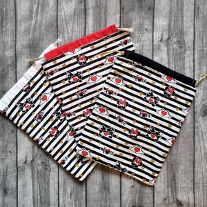 Op de afbeelding: Drie zwart-wit gestreepte stoffen tassen met een rood, wit en zwart Mickey Mouse en Minnie Mouse ontwerp. De tassen hebben gouden glitteraccenten en de woorden "Love" erop gedrukt.