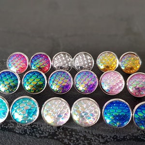 Könnte beinhalten: Sortiment von 12 regenbogenfarbenen Ohrsteckern mit Meerjungfrauen-Schuppen in verschiedenen Farben, darunter Pink, Blau, Grün, Lila, Silber und Gold.