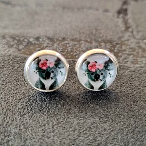 Op de afbeelding: Een paar zilveren oorbelletjes met een ronde glazen cabochon met daarop een koala die een bloemenkrans draagt. De koala is grijs met een witte borst en zwarte ogen. De bloemen zijn roze en groen.