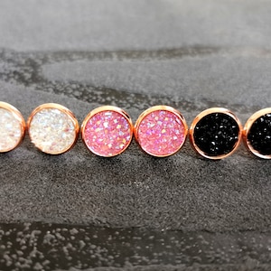 Könnte beinhalten: Sechs Paare kleiner runder Ohrringe mit einer Roségoldfassung. Die Ohrringe bestehen aus Glitzer, der in Harz eingebettet ist. Die Farben des Glitzers sind Weiß, Rosa und Schwarz.