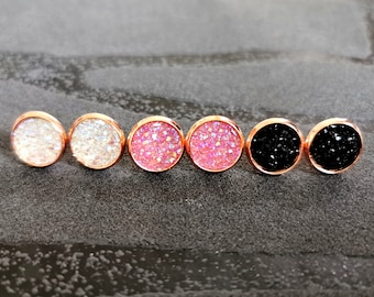May include: Six pairs of small round earrings with a rose gold setting. The earrings are made of glitter embedded in resin. The colors of the glitter are white, pink, and black.