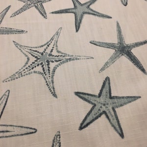 May include: A white fabric with a repeating pattern of blue starfish. The starfish are different sizes and are scattered randomly across the fabric.