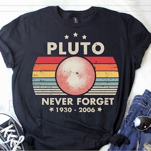May include: Black t-shirt with a retro-style graphic of Pluto, a planet with a red-orange color, and the text "Pluto Never Forget 1930 - 2006".