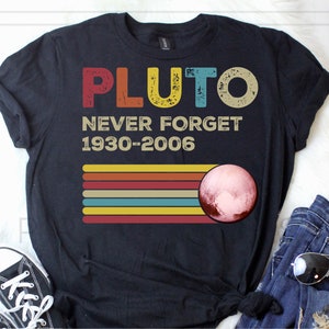 May include: Black t-shirt with a vintage-style graphic that says "Pluto Never Forget 1930-2006". The graphic features a red, orange, yellow, and blue striped design with a pink and brown planet in the center.