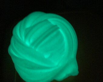 May include: A close-up of a bright green glow-in-the-dark slime. The slime is in a large, round shape and has a smooth, glossy texture.