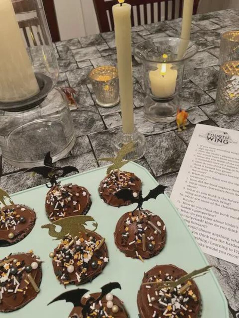 K&ouml;nnte beinhalten: Eine Halloween-Dessert-Pr&auml;sentation mit schokoladen&uuml;berzogenen Leckereien, die mit Streuseln und fledermausf&ouml;rmigen Aufs&auml;tzen verziert sind. Angez&uuml;ndete Kerzen und dekorative Kerzenhalter tragen zur gruseligen Atmosph&auml;re bei.