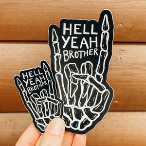 May include: Two black and white skeleton hand stickers with the text "Hell Yeah Brother" in white. The larger sticker is held in a hand.