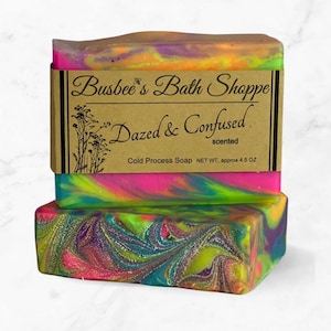 Op de afbeelding: Twee handgemaakte zeepstaven met een swirl van roze, groen, geel en blauwe kleuren. De zeep is gelabeld "Busbee's Bath Shoppe Dazed & Confused scented Cold Process Soap NET WT. approx 4.5 OZ"