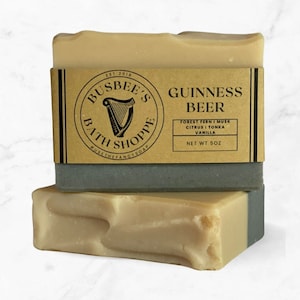 May include: Image of two bars of soap, one on top of the other. The top bar has a brown paper label with black text that reads 'EST 2018 BUSBEE'S BATH SHOPPE #USETHEFANCYSOAP GUINNESS BEER FOREST FERN I MUSK CITRUS I TONKA VANILLA NET WT 5OZ'.