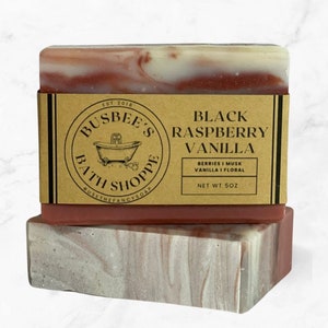 May include: Two bars of handmade soap. The top bar is labeled "Black Raspberry Vanilla" with a brown label. The soap has a layered design with red, white, and brown swirls. The net weight is 5 oz.