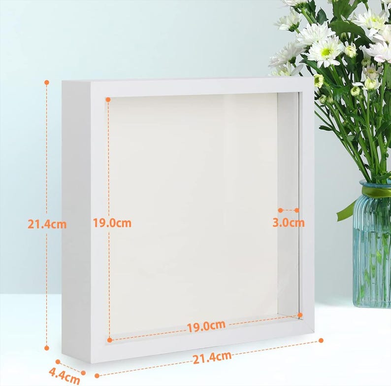 May include: A square white shadow box frame with a clear front panel. The frame has an outer height and width of 21.4 cm, an inner display area of 19.0 cm by 19.0 cm, a depth of 4.4 cm, and an inner depth of 3.0 cm as indicated by measurements.