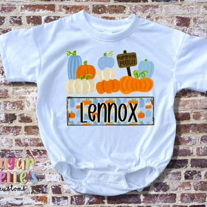 May include: White baby bodysuit featuring a pumpkin patch design. The design includes orange, white, and blue pumpkins, a sign that says "Pumpkin Patch", and the name "Lennox".