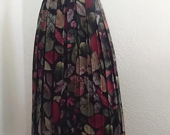 May include: A pleated midi skirt with a leaf pattern in red, green, and brown on a black backdrop. The skirt is displayed on a mannequin, showing its full length and design. The skirt's length is approximately 70 cm.
