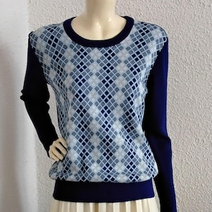 Könnte beinhalten: Ein Pullover im Vintage-Stil mit einem blau-weißen Rautenmuster auf Brust und oberem Rücken. Die Ärmel und der Saum sind marineblau. Dazu ein langer, plissierter cremefarbener Rock. Das Outfit wird auf einer Schaufensterpuppe präsentiert.
