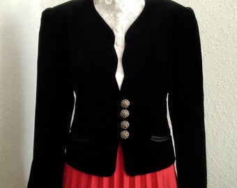 May include: A black velvet blazer with a V-neckline and four silver buttons. The blazer is worn over a white lace blouse and a red pleated skirt.