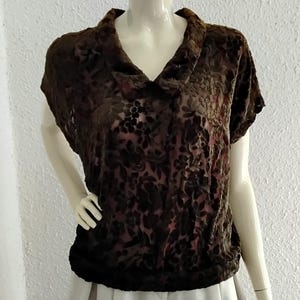 Könnte beinhalten: Braunes Oberteil mit kurzen Ärmeln, Wasserfallausschnitt und floralem Muster. Das Oberteil ist aus einem samtartigen Material gefertigt und wird mit einem hellen Rock kombiniert. Die Schaufensterpuppe wird vor einer weißen Wand präsentiert.