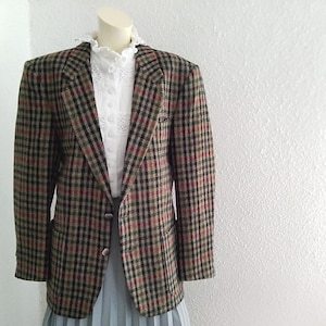 Pode incluir: Um blazer xadrez marrom, preto e vermelho com um fecho de botão único. O blazer tem um bolso do lado esquerdo.