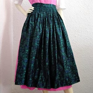 Könnte beinhalten: Ein hoch taillierter, plissierter Midirock mit einem floralen Jacquardmuster in Dunkelblau und Smaragdgrün. Der Rock hat einen breiten, strukturierten Bund und eine volle, voluminöse Silhouette, die unter die Knie fällt, über einem leuchtend rosa Unterrock.
