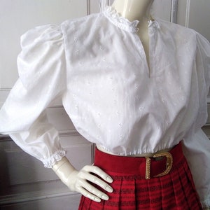 May include: White eyelet blouse with puffed sleeves and a gathered elastic waistband. The blouse has a V-neckline and a lace trim around the collar.