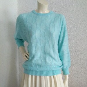 以下が含まれることがあります： テクスチャパターンが付いた薄いブルーのセーター。セーターは長袖でクルーネックです。