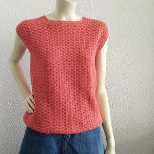 May include: A coral pink sleeveless knitted top with a textured pattern. The top has a round neckline and a slightly cropped length.