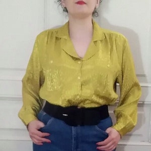 Peut inclure: Une femme porte un chemisier en satin jaune avec une ceinture noire et un jean bleu. Elle porte des ballerines rouges.