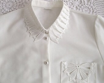 May include: White button-up shirt with a delicate lace collar and a lace pocket detail.
