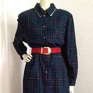 May include: A navy, green, and pink plaid dress with gold threads. The dress has a white-trimmed collar, long sleeves, and a red belt with a gold buckle. The dress is displayed on a mannequin. The dress is approximately 100 cm in length.