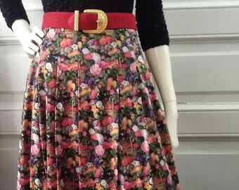 May include: A black sweater with a lace neckline and a red belt. The sweater is worn over a floral print skirt with a pleated design.