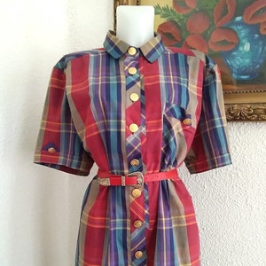 May include: A red, blue and yellow plaid dress with a collared neckline and short sleeves. The dress has a gold button fastening and a red belt with a gold buckle.