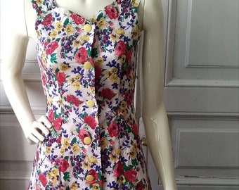 May include: A sleeveless white dress with a floral print in shades of red, yellow, and purple. The dress has a button-up front and a fitted silhouette.