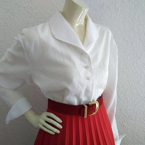 May include: A white collared blouse with long sleeves and a red pleated skirt with a gold belt.