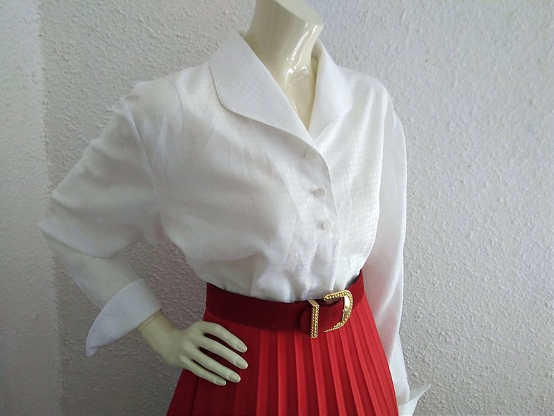 May include: A white collared blouse with long sleeves and a red pleated skirt with a gold belt.