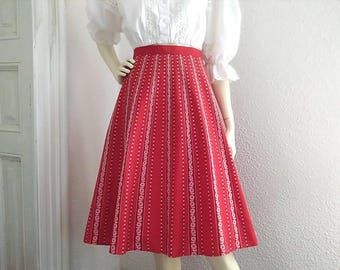 Pode incluir: Uma saia vermelha e branca com padrão, com uma silhueta completa e de linha A. A saia tem listras verticais e um design floral branco.