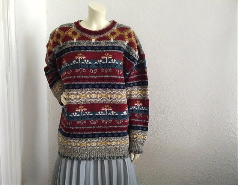 May include: A multi-colored sweater with a geometric pattern in shades of red, blue, yellow, and white. The sweater has a crew neck and long sleeves.