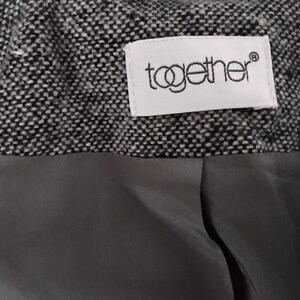 May include: Close-up of a garment's interior, showing a textured black and white tweed fabric. A grey lining is visible below the tweed. A white label with the word "together" is sewn into the tweed.