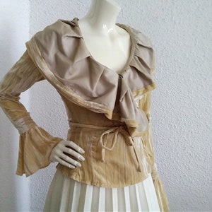 May include: A long-sleeved, gold velvet blouse with a large, ruffled collar and a tie at the waist.