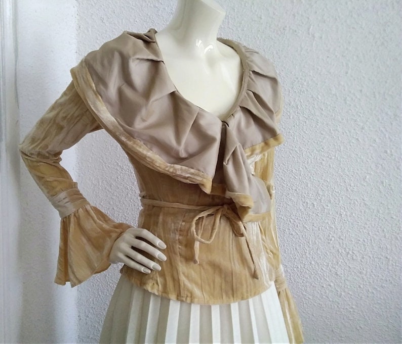 May include: A long-sleeved, gold velvet blouse with a large, ruffled collar and a tie at the waist.