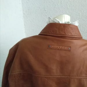 May include: A brown leather jacket with a Pierre Cardin label on the back.