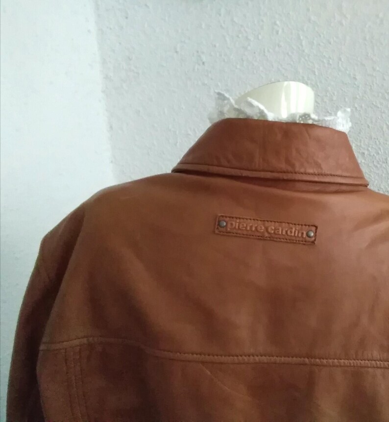 May include: A brown leather jacket with a Pierre Cardin label on the back.