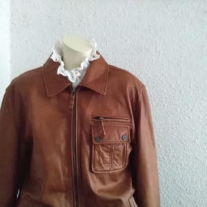 May include: A brown leather jacket with a zipper closure and a large pocket on the front.