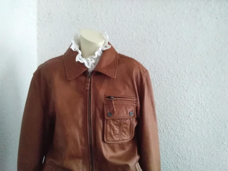 May include: A brown leather jacket with a zipper closure and a large pocket on the front.