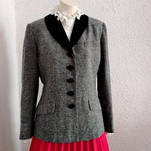 May include: A grey tweed jacket with a black velvet collar and black buttons. The jacket is worn with a white blouse with a lace collar and a bright pink pleated skirt. A classic, elegant outfit.