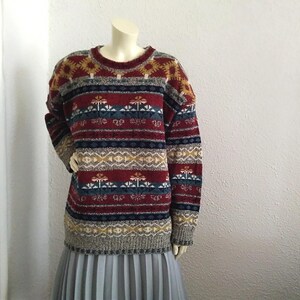 May include: A colorful striped sweater with a geometric pattern in shades of red, blue, yellow, and white. The sweater has a crew neck and long sleeves.