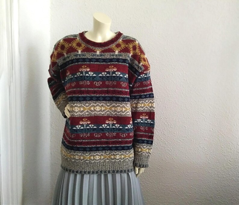 May include: A colorful striped sweater with a geometric pattern in shades of red, blue, yellow, and white. The sweater has a crew neck and long sleeves.