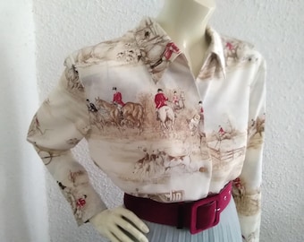 May include: A white long-sleeved button-down shirt with a brown and red print of people riding horses. The shirt has a collar and a red belt.