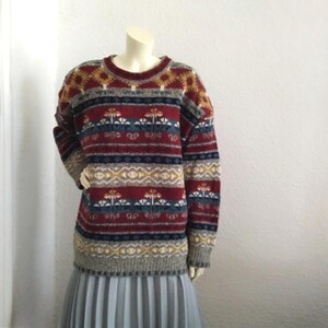 May include: A colorful striped sweater with a geometric pattern in shades of red, blue, yellow, and gray. The sweater has a crew neck and long sleeves.