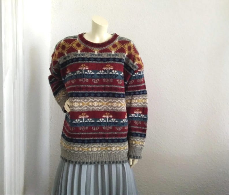 May include: A colorful striped sweater with a geometric pattern in shades of red, blue, yellow, and gray. The sweater has a crew neck and long sleeves.